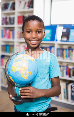 Scolaro holding globe in libreria Foto Stock