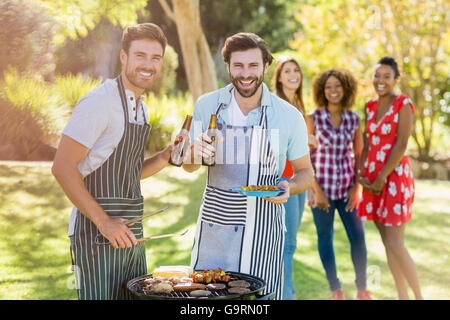 Due uomini in possesso di una bottiglia di birra mentre prepara barbecue grill Foto Stock