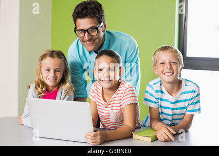 Insegnanti e bambini usando computer portatile in biblioteca Foto Stock