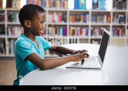 Scolaro utilizzando laptop in biblioteca Foto Stock