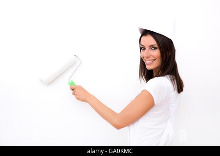 Una giovane e bella donna adulta pittura un muro nella sua abitazione in bianco. Foto Stock