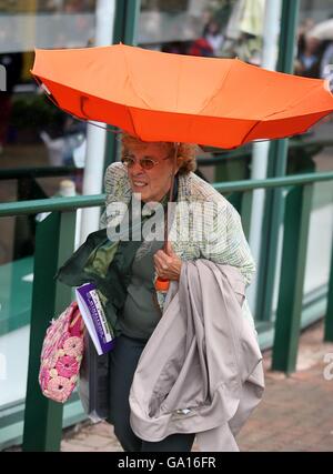 Tennis - Wimbledon Championships 2007 - Day One - All England Club. Un tifoso del tennis cammina sopra mentre il suo ombrello soffia dentro fuori Foto Stock
