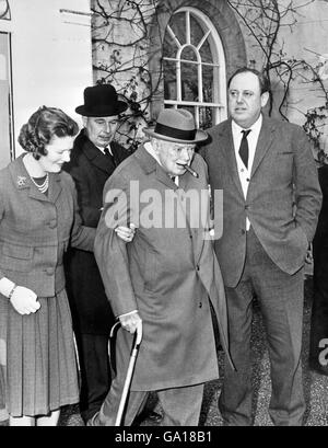 Sir Winston Churchill, l'inevitabile sigaro tra le labbra, ottiene una mano d'aiuto affettuosa da sua figlia, Mary, e dal genero Christopher Soames, mentre lascia la loro casa georgiana a Hamsell Manor, Eridge Green, vicino a Tunbridge Wells. Con Lady Churchill era stato ospite di un pranzo di famiglia per festeggiare il suo 79° compleanno. Avevano scacciato dalla loro casa a Chartwell, Kent Foto Stock