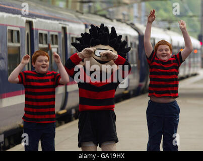 Dennis The Menace affiancato dai gemelli John (a sinistra) e Andrew Muirhead alla stazione di Waverly, Edimburgo, per lanciare il primo viaggio gratuito ScotRail ogni fine settimana con i biglietti per la famiglia Funday. Foto Stock