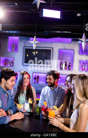 Gruppo di amici interagire gli uni con gli altri al bancone mentre avente cocktail Foto Stock