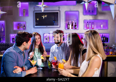 Gruppo di amici interagire gli uni con gli altri al bancone mentre avente cocktail Foto Stock