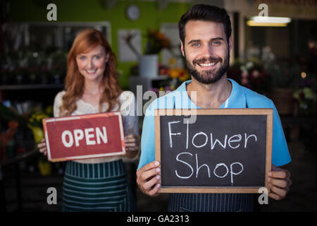 Uomo con ardesia con negozio di fiori segno e donna tenendo aperte cartello Foto Stock