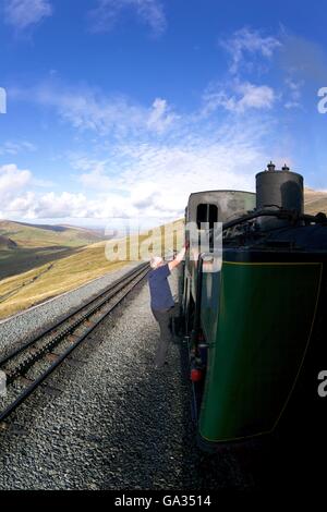 Autista si arrampica sul motore di vapore sul viaggio fino Snowdon Mountain Railway, Parco Nazionale di Snowdonia, Gwynedd, Wales, Regno Unito, GB, Europa Foto Stock