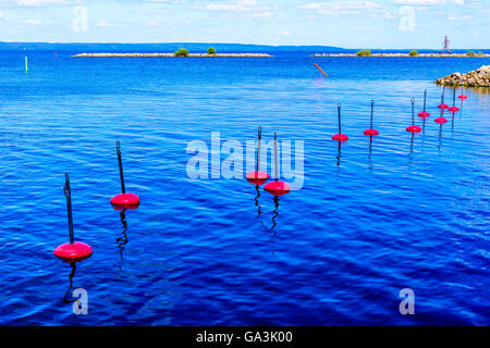 Fila di red boe di ormeggio in mare con marcata per via navigabile in background. Foto Stock