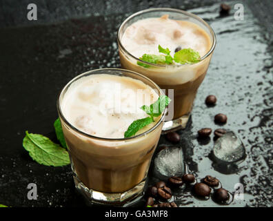Caffè ghiacciato in bicchieri con cubetti di ghiaccio e foglie di menta fresca e caffè in grani Foto Stock