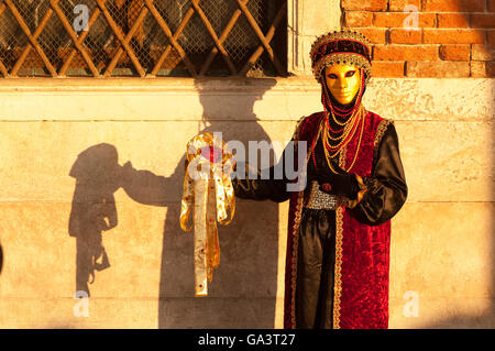 In Masketeers decorativo sontuoso velluto rosso con perle costume inondate di luce calda del sole e ombra sulla parete in corrispondenza della maschera di Venezia festival Foto Stock