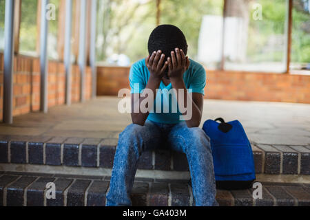 Triste schoolboy seduto da solo sulla scala Foto Stock
