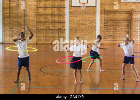 Gli studenti a giocare con hula hoop nella palestra della scuola Foto Stock