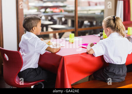 Un ragazzo e una ragazza in uniformi di scuola a pranzo in mensa scolastica Foto Stock