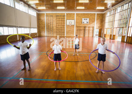 Gli studenti a giocare con hula hoop nella palestra della scuola Foto Stock