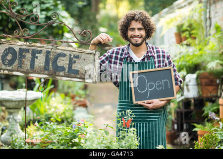 Giardiniere maschio tenendo aperte segno dalla targhetta di office Foto Stock