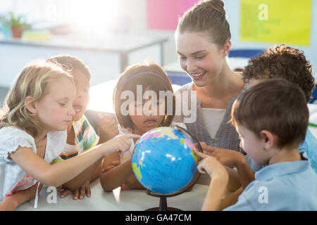 Insegnante guardando scolari toccando globe Foto Stock