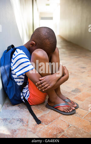 Triste ragazzo seduto sul corridoio a scuola Foto Stock