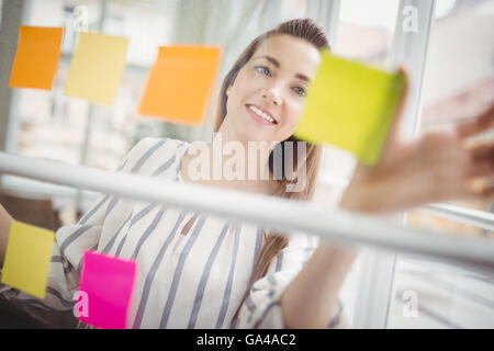 Felice imprenditrice guardando note adesive in ufficio creativo Foto Stock