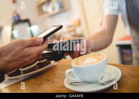Close-up del cliente con il cellulare e il barista con lettore di schede Foto Stock