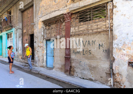 Scena di strada con la gente del luogo in chat tra gli edifici dilapitated in Inquisidor Street, Habana Vieja, Old Havana, Cuba Foto Stock