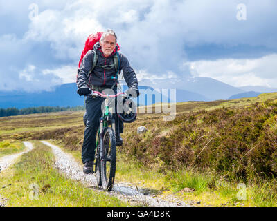 Uomo in pensione su una bici da corsa di imballaggio attraverso le Highlands scozzesi Foto Stock