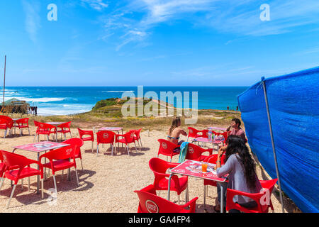 PRAIA DO AMADO Beach, Portogallo - 15 Maggio 2015: turisti seduti in un caffè sulla spiaggia Praia do Amado spiaggia con vista oceano in background, regione di Algarve, Portogallo. Foto Stock