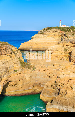 Vista delle scogliere di roccia con il faro in distanza, Algarve, PORTOGALLO Foto Stock