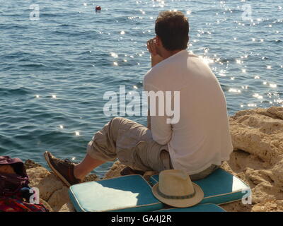 Giovane uomo seduto sulle rocce guardando il tramonto,Rovigno Croazia Foto Stock