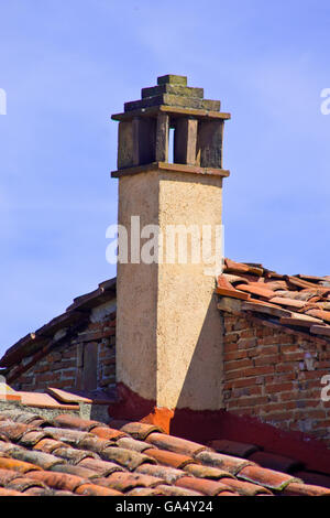 Camino in stucco e mattoni, sulle tegole del tetto di un edificio tradizionale Foto Stock