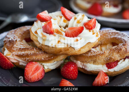 Soffio di crema anelli (bignè) decorate con fragole fresche e salsa di caramello Foto Stock