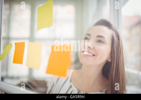 Sorridente imprenditrice guardando note adesive in ufficio creativo Foto Stock
