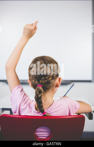Vista posteriore del schoolgirl alzando la mano in aula Foto Stock
