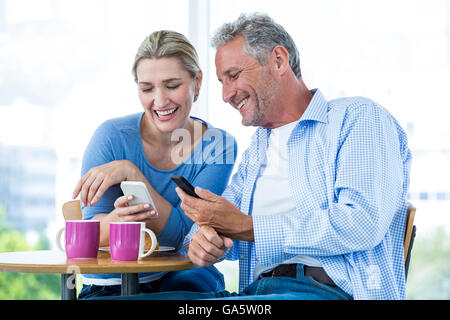Coppia sorridente utilizzando i telefoni cellulari al cafe Foto Stock