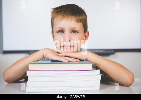 Ritratto di ragazzo sorridente appoggiato sulla pila di libri in camera di classe Foto Stock