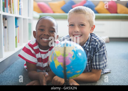 Ritratto di ragazzi in età scolare studiando globo in biblioteca Foto Stock