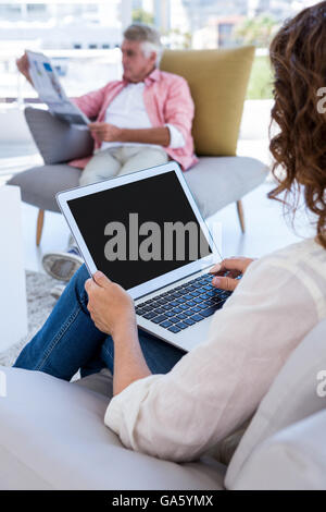 Donna che utilizza computer portatile mentre uomo maturo quotidiano di lettura Foto Stock