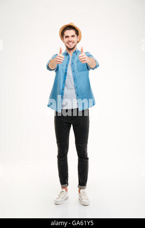 A piena lunghezza ritratto allegro giovane uomo che mostra pollice in alto isolato su sfondo bianco Foto Stock