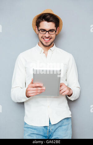 Ritratto di un felice giovane uomo in occhiali utilizzando computer tablet isolata su uno sfondo grigio Foto Stock
