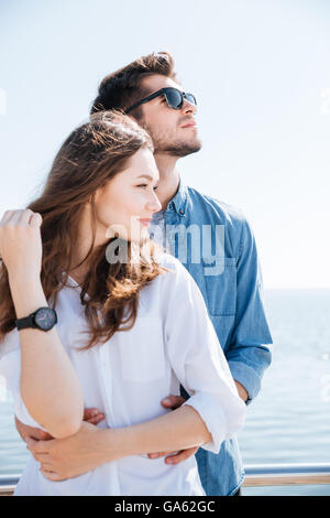 Ritratto di una giovane coppia in piedi insieme abbracciando e cercando di distanza al mare Foto Stock