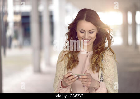 Moda giovane donna in nero cappotto e sciarpa colorata occupato con il suo telefono cellulare mentre si cammina per una via della città Foto Stock