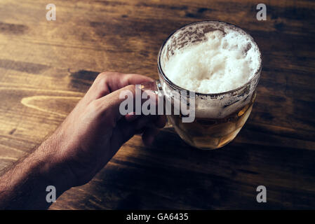 Mano azienda boccale di birra piena di freddo fresco drink alcolici su sfondo di legno, uomo nel bar, pov shot, il fuoco selettivo Foto Stock