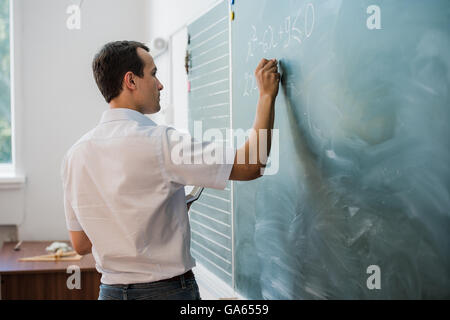 Giovane maschio insegnante o studente azienda chalk scrivere sulla lavagna in aula Foto Stock