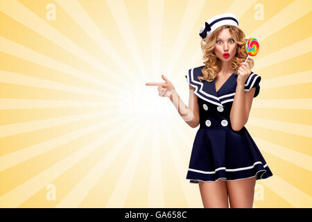 Sorpreso pin-up sailor ragazza con un lecca-lecca da parte di puntamento in stile cartoon sfondo. Foto Stock