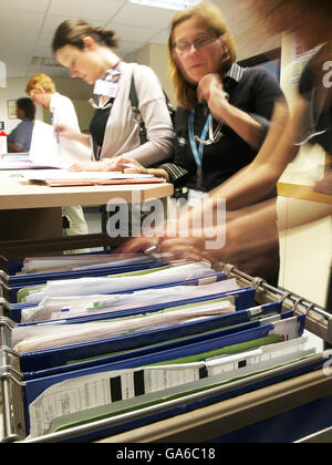 Note paziente con il personale medico a piedi in background e medici di esplorazione file medici su occupato ward nel grande ospedale generale Foto Stock