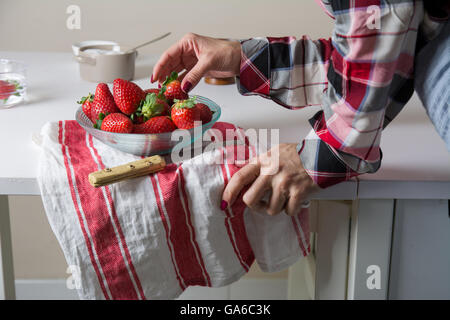 La donna la raccolta di fragole, una ciotola di vetro, in piedi accanto alla tavola Foto Stock