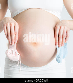 Una donna bregnant detiene una rosa bootie e uno blu bootie nella parte anteriore del suo bambino bump. Foto Stock