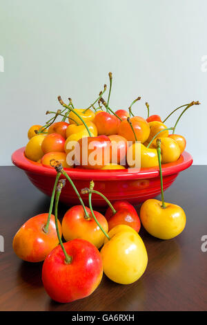 Pila di ciliegie Rainier in una ciotola rossa seduta su una tavola di legno Foto Stock