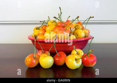 Pila di ciliegie Rainier in una vaschetta di colore rosso e su un tavolo di legno closeup Foto Stock