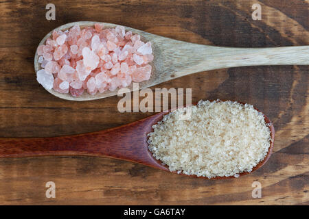 Il sale e lo zucchero in cucchiai di legno vista dall'alto. Rosa himalayano sale di roccia e di zucchero greggio di canna. Foto Stock